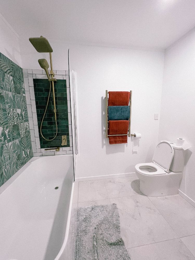 White bathroom with green tiles, brass shower and heated towel rail